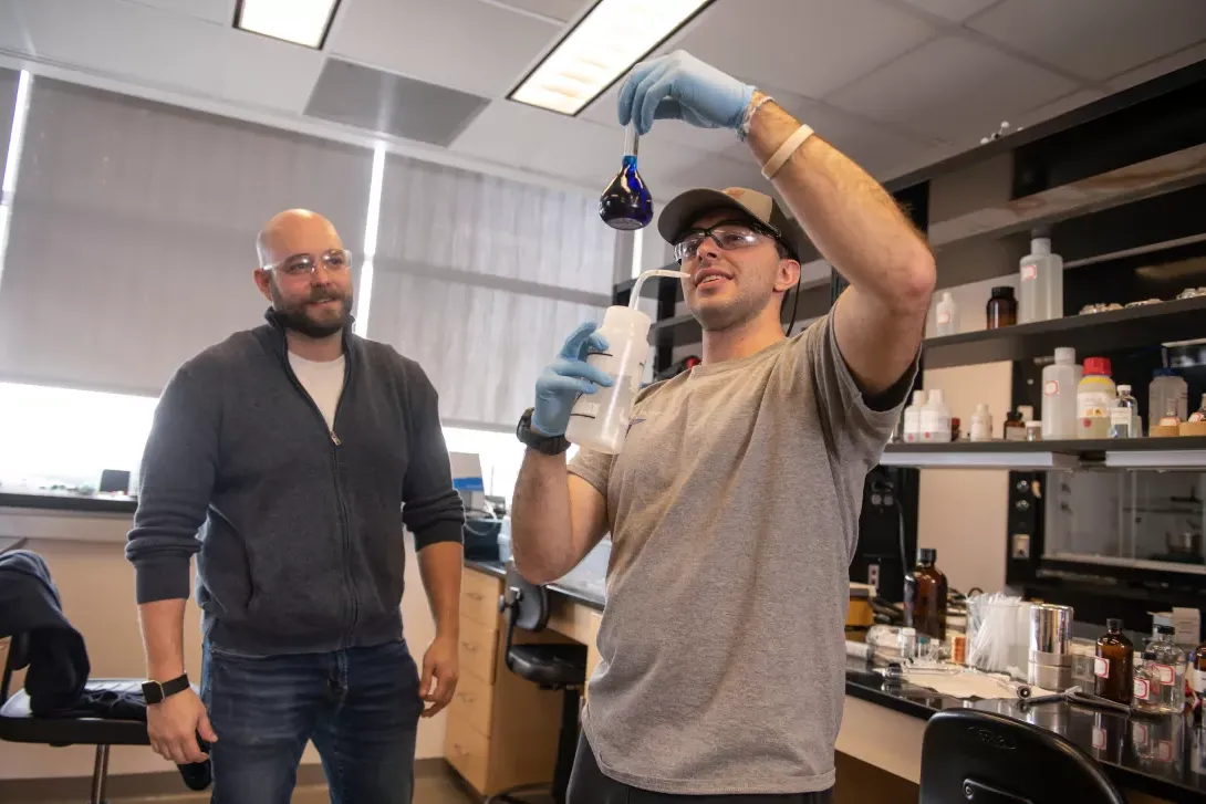 Student performing an experiement in chemistry lab while instructor supervises